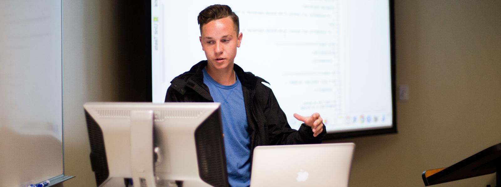 student looks at computer screen while giving class presentation
